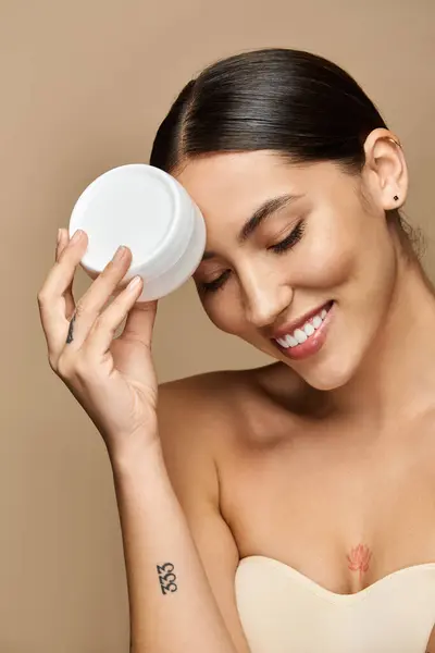 Brunette woman happily applies moisturizing cream while embracing self care in a calm atmosphere. — Stock Photo