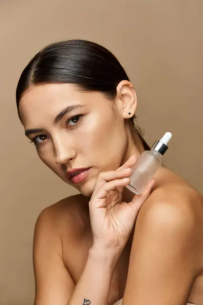 Young woman holds skincare serum against a warm, neutral background while highlighting her beauty. — Stock Photo