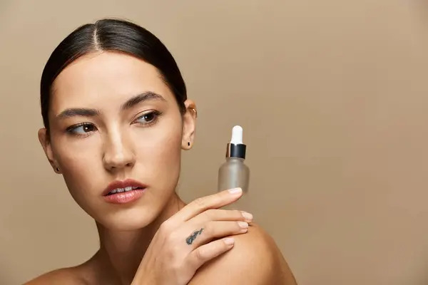 Brunette woman gracefully holds a beauty serum, exuding confidence in soft light. — Stock Photo