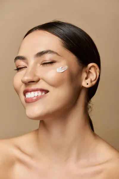 Beautiful brunette woman applies cream on her cheek, radiating confidence and joy while smiling. — Stock Photo