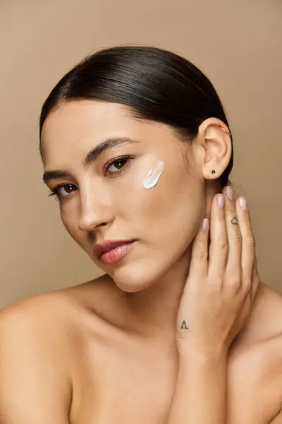 Young brunette woman gently applying a cream to her cheek, radiating confidence and beauty. — Stock Photo