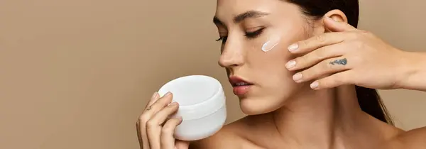 Uma jovem aplica creme ao rosto, irradiando serenidade e beleza natural. — Fotografia de Stock