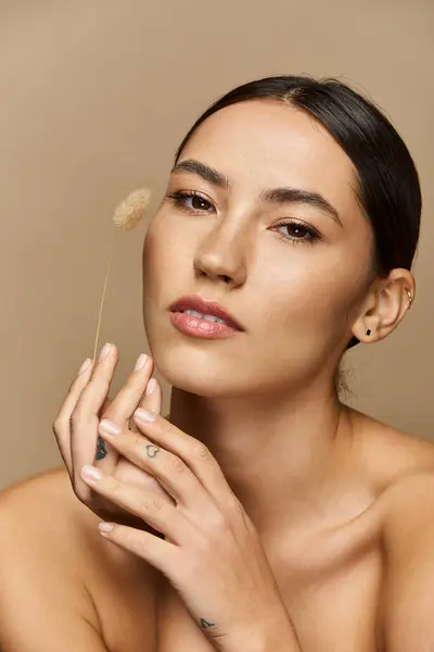 Young woman with brunette hair gently holds a spikelet while showcasing her natural beauty indoors. — Stock Photo