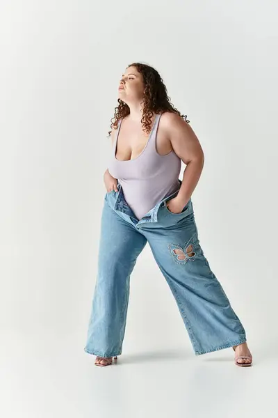 Young woman confidently poses in oversized jeans and a fitted top against a minimalist backdrop. — Stock Photo