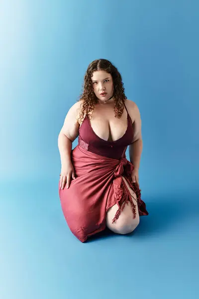 A young woman showcases her fashion sense while kneeling elegantly on a soft blue surface. — Stock Photo