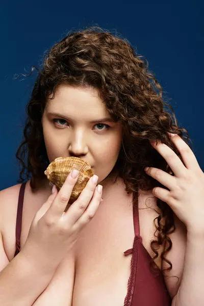 Una mujer joven disfruta de un aperitivo de concha marina mientras muestra su atuendo de moda y su estilo único. - foto de stock