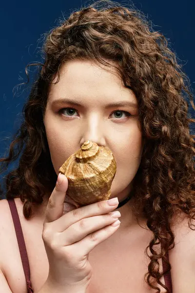 A trendy young woman with curly hair holds a seashell, flaunting her unique style. — Stock Photo