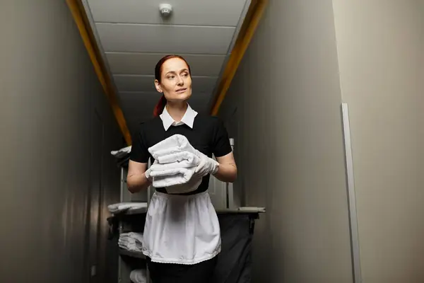 A young woman walks through a quiet hallway, holding neatly folded towels with grace. — Stock Photo