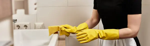 A young woman diligently wipes down the sink and countertop in her kitchen, showcasing her focus. — Stock Photo