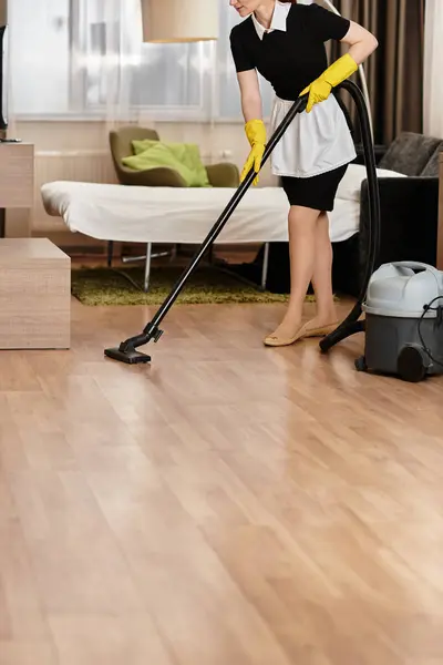 Uma mulher bonita em uma roupa preto e branco aspira o chão de uma elegante sala de estar. — Fotografia de Stock