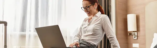 Smiling woman engages in work from her laptop while seated comfortably in a hotel room. — Stock Photo