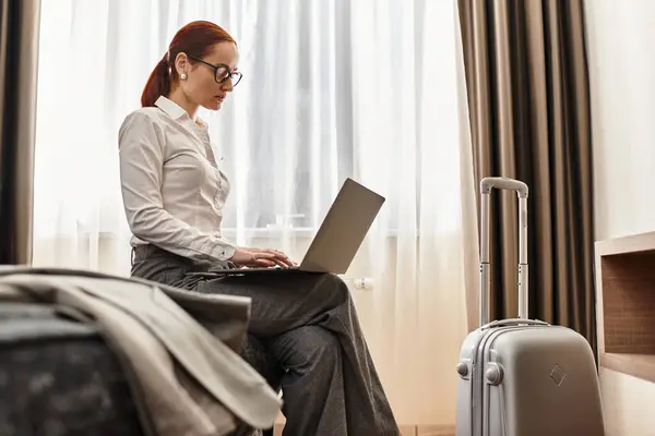 A young woman intently types on her laptop while seated in a stylish hotel room. — Stock Photo