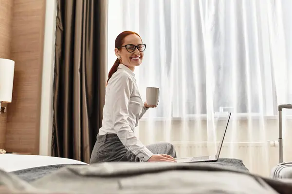Cheerful young woman drinks coffee and works on her laptop in a bright, modern room. — Stock Photo