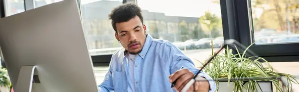 Un hombre guapo se concentra en tareas en una oficina vibrante rodeada de luz solar y plantas. - foto de stock