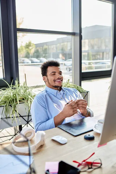 Smiling man sits at a desk, engaging with his work in a modern and airy office environment. — Stock Photo