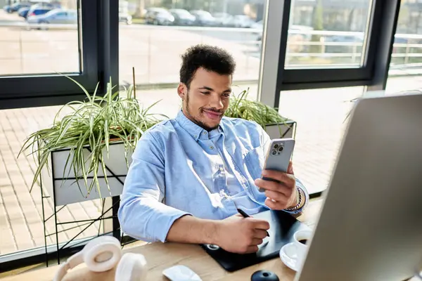 Un hombre guapo disfruta de su tiempo en un espacio de trabajo moderno mientras usa su teléfono inteligente y tableta. - foto de stock