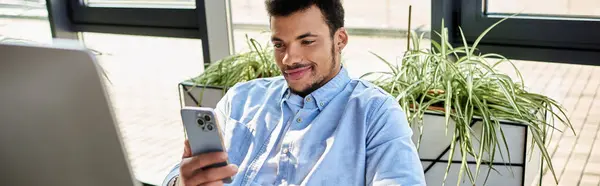 A handsome man relaxes while browsing his smartphone in a stylish office filled with plants. — Stock Photo