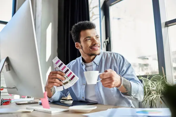 Handsomeness radiates as a man sips coffee and chooses color palettes in a stylish workspace. — Stock Photo