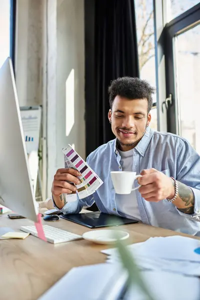 Ein stilvoller Mann hält eine Farbpalette und eine Kaffeetasse an seinem Schreibtisch in kreative Arbeit vertieft. — Stockfoto