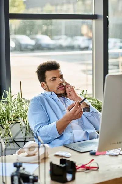 Engaged in a phone call, a handsome man contemplates while seated at a stylish desk. — Stock Photo