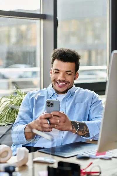 Ein fröhlicher Mann lächelt breit, als er an einem modernen Arbeitsplatz mit seinem Smartphone hantiert. — Stockfoto