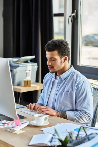 Un bell'uomo digita intensamente sul suo computer in uno spazio di lavoro ben illuminato, circondato dalla creatività. — Foto stock