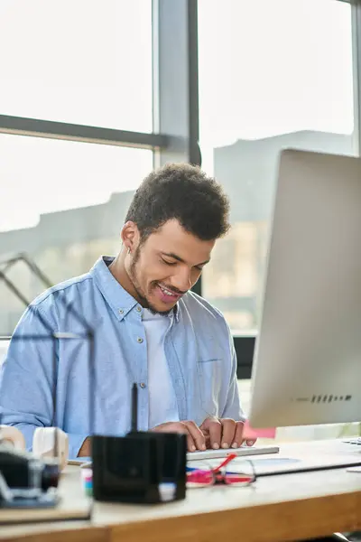 Man smiles while typing on a laptop at a stylish workspace filled with sunlight. — Stock Photo