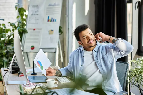 Young man happily chats on the phone at his tidy desk during the day. — Stock Photo