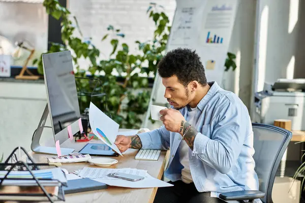 Handsome man reviews colorful charts and graphs while enjoying coffee in a bright workspace. — Stock Photo