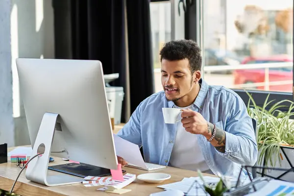 This charming man sips coffee at his modern, green filled workspace while engaging in tasks. — Stock Photo