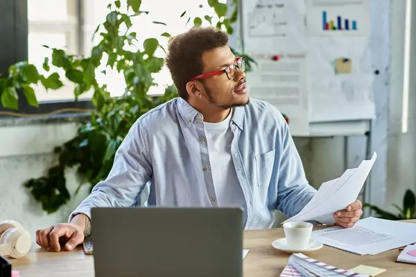 Handsome man wearing stylish glasses examines papers in an inspiring, sunlit office environment. — Stock Photo
