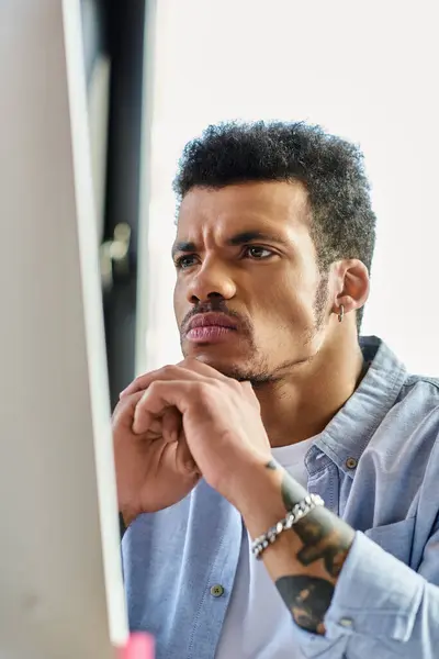 A handsome man sits thoughtfully at his desk, engaged in computer work during daylight. — Stock Photo