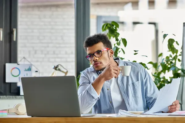 Handsome man reviews important documents with coffee in hand at a stylish workspace. — Stock Photo
