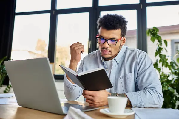 Handsome man in glasses reading from a notebook at a stylish workspace with plants around him. — Stock Photo