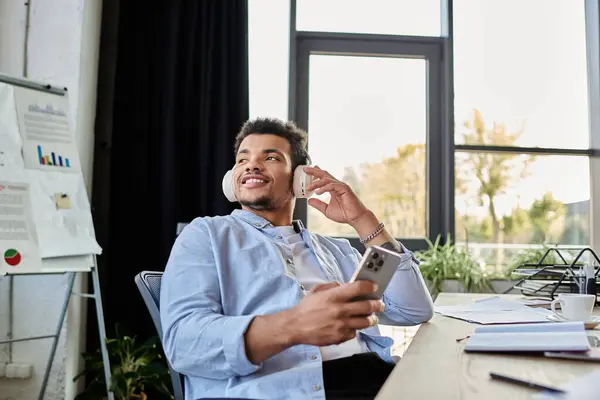 Un uomo elegante ascolta musica con le cuffie mentre lavora su una scrivania di legno. — Foto stock