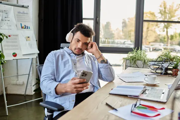 Man listens to music with headphones while looking at his phone in a stylish workspace. — Stock Photo