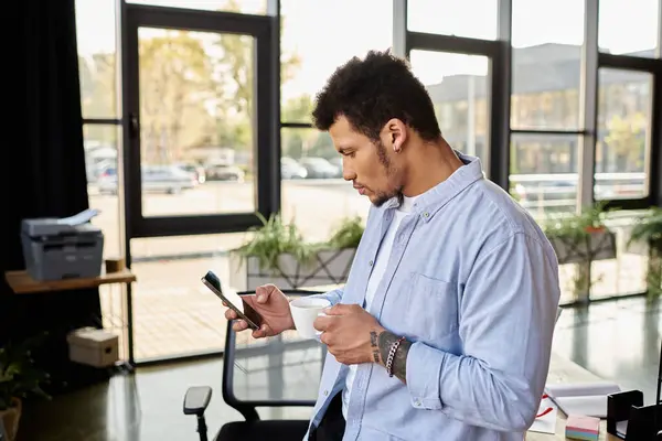 Smartly dressed man in a bright workspace enjoys coffee while engaging with his smartphone. — Stock Photo