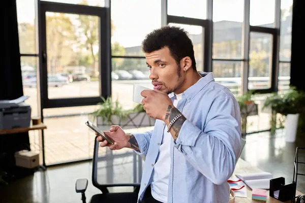 Handsome individual sipping coffee and browsing his smartphone in a stylish workspace. — Stock Photo
