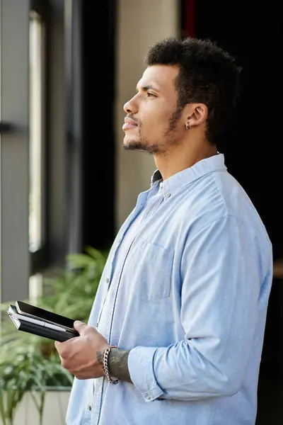 A handsome man stands near a window, contemplating with a notebook in hand, lost in thought. — Stock Photo