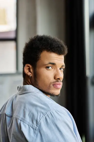 A stylish man with curly hair looks back with a contemplative expression in a bright room. — Stock Photo