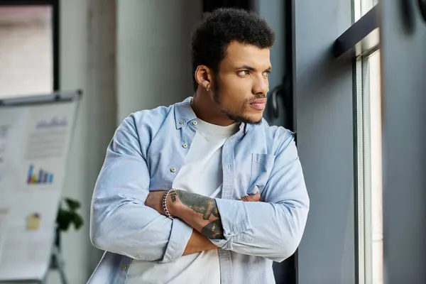 A handsome man stands thoughtfully by a window, arms crossed in a chic office setting. — Stock Photo