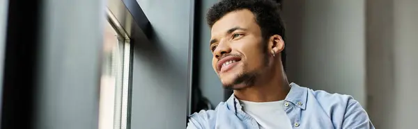 Young man leans by the window, smiling while contemplating his thoughts in a warm atmosphere. — Stock Photo