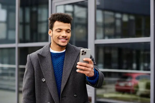 Ein gutaussehender Mann ist mit seinem Smartphone beschäftigt und lächelt in einer städtischen Umgebung. — Stockfoto