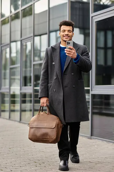 Ein stilvoller Mann schlendert durch ein modernes Stadtgebiet, beschäftigt mit seinem Handy und verströmt Charme. — Stockfoto