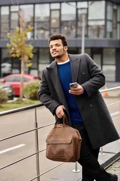 Stylishly dressed man stands by a railing, holding a phone and savoring the urban vibe. — Stock Photo
