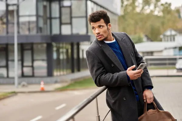 Stylish man stands in an urban environment, absorbed in his phone in the afternoon light. — Stock Photo