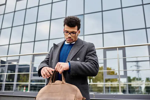 Handsome man adjusts his bag while standing near a contemporary glass building under a cloudy sky. — Stock Photo