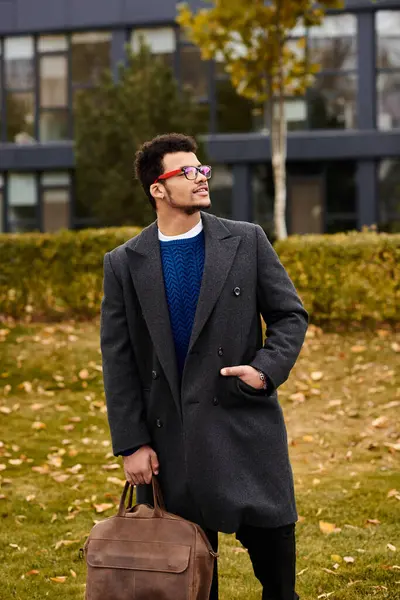 Hombre guapo se para con confianza con una bolsa, apreciando la belleza de las hojas de otoño. — Stock Photo