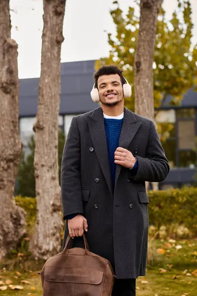 Un uomo elegante sorride mentre cammina attraverso un paesaggio autunnale, vestito per il clima fresco. — Foto stock