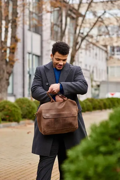 Man dressed warmly enjoys a moment outdoors, looking into a stylish bag with a smile. — Stock Photo